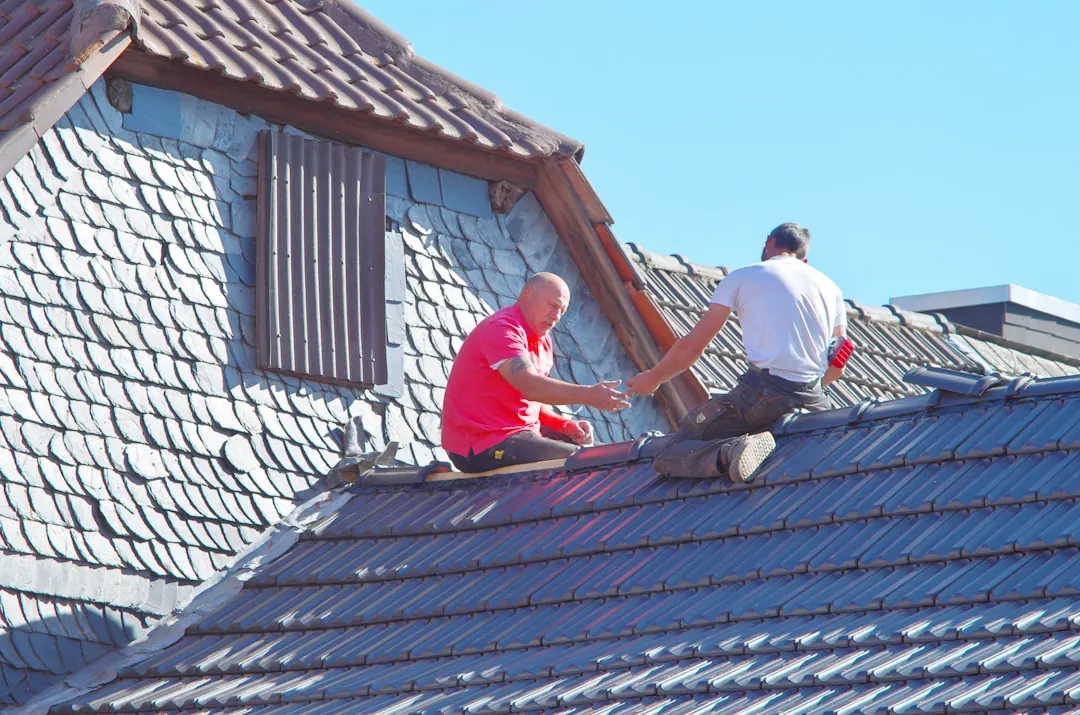 Dva pokrývači opravují krytinu na střeše domu